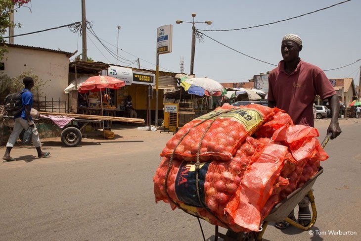 man pushing vegetables on a wheelbarrow to market